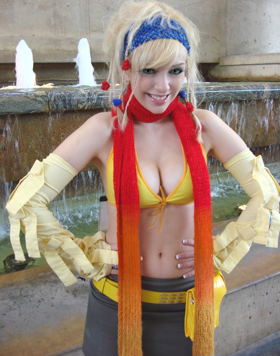 1girl, bare_shoulders, belt, bikini, blonde_hair, breasts, cosplay, cosplay_photo, cowboy_shot, elbow_gloves, facing_viewer, female_focus, final_fantasy, final_fantasy_x, final_fantasy_x-2, fingerless_gloves, fountain, front-tie_bikini_top, front-tie_top, gloves, gradient_scarf, hands_on_own_hips, lip_gloss, looking_at_viewer, makeup, mascara, medium_breasts, midriff, navel, otakon, pale_skin, photo_(medium), rikku_(ff10), rikku_(ff10)_(cosplay), scarf, smile, solo, standing, swimsuit, yellow_belt, yellow_bikini, yellow_gloves