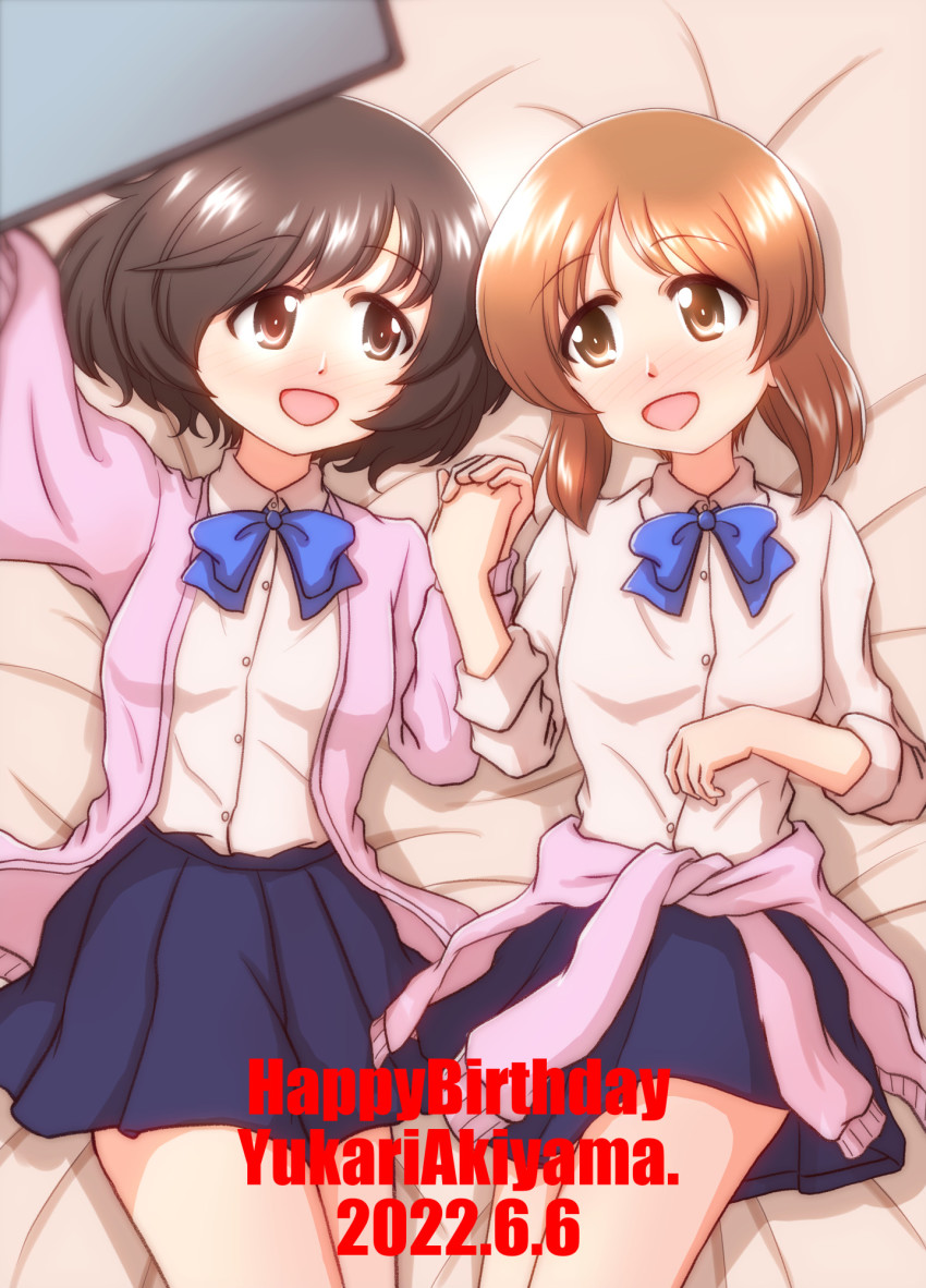 2022, 2girls, akiyama_yukari, alternate_costume, bed_sheet, birthday, blue_ribbon, cellphone, clothes_around_waist, dated, girls_und_panzer, happy_birthday, highres, holding, ishitsu_tadashi, jacket, jacket_around_waist, lying, miniskirt, multiple_girls, nishizumi_miho, phone, pink_jacket, ribbon, selfie, skirt, smartphone, yuri