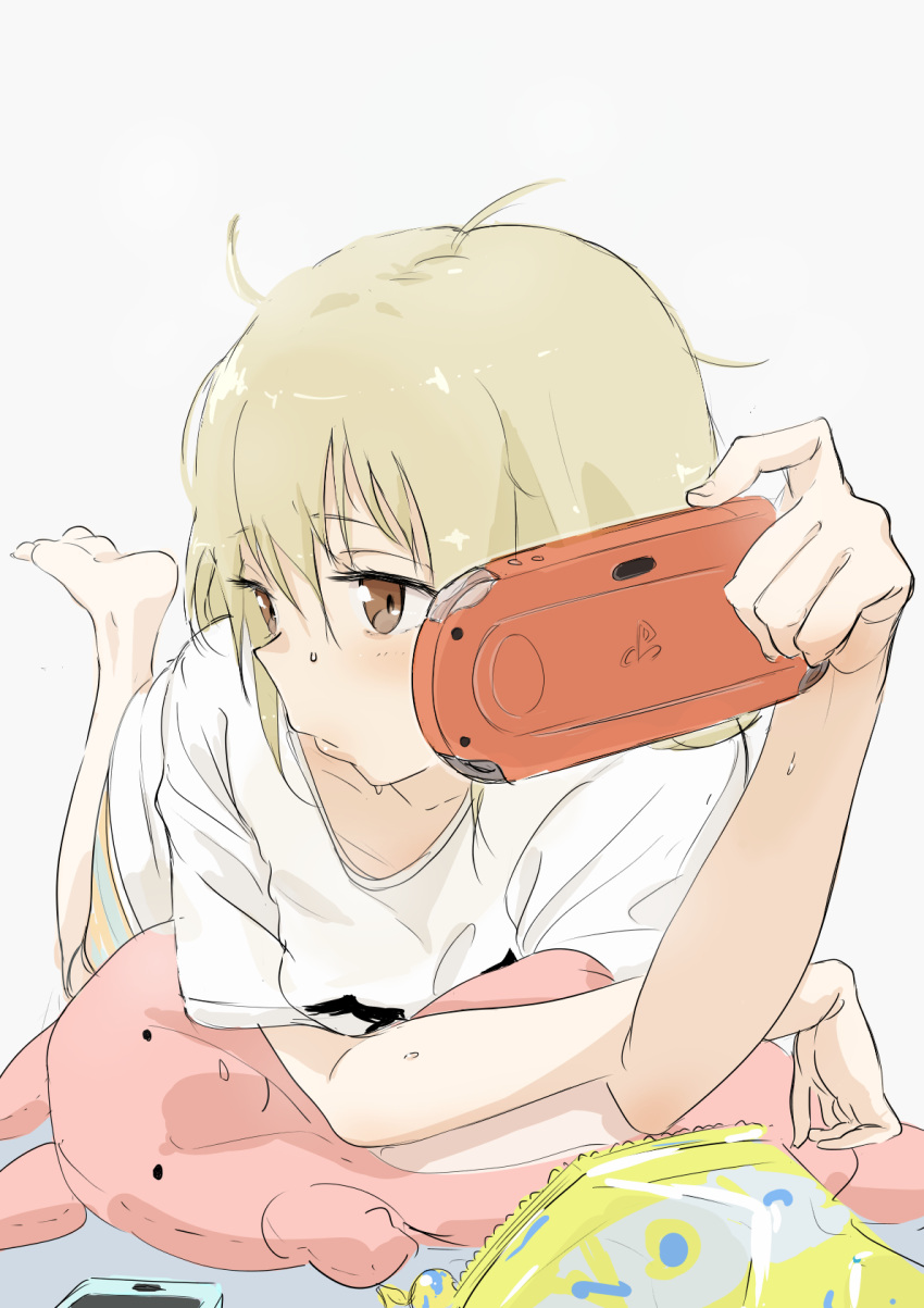 1girl, bag_of_chips, bangs, barefoot, blonde_hair, blush, bouen, brown_eyes, cellphone, closed_mouth, eyebrows_visible_through_hair, feet_up, futaba_anzu, grey_background, hair_between_eyes, handheld_game_console, highres, idolmaster, idolmaster_cinderella_girls, lips, long_hair, looking_to_the_side, lying, messy_hair, on_stomach, phone, playstation_portable, shirt, short_sleeves, simple_background, smartphone, solo, stuffed_animal, stuffed_bunny, stuffed_toy, t-shirt