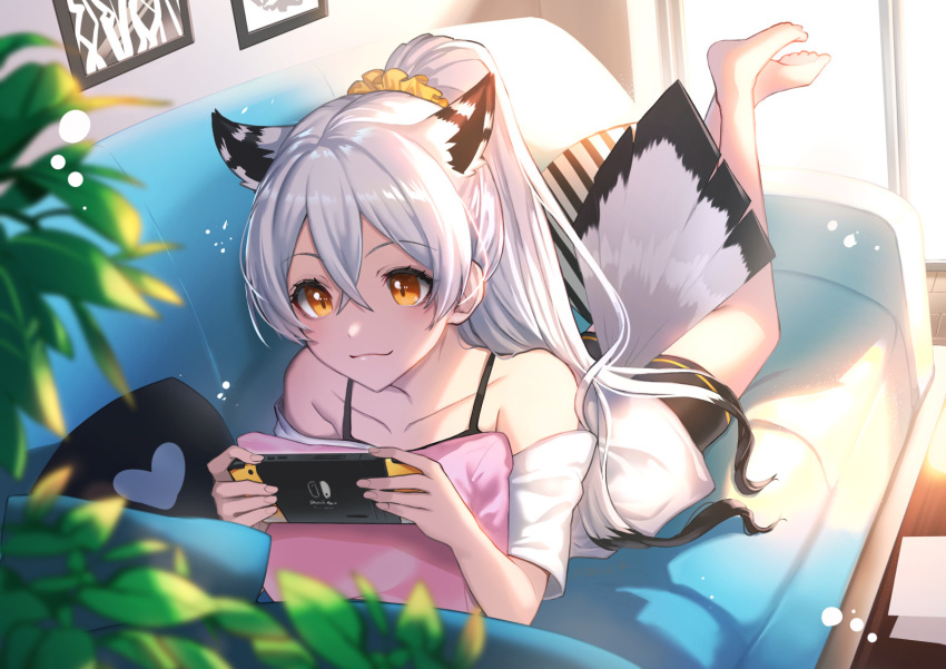 1girl, animal_ears, bangs, bare_shoulders, barefoot, black_hair, black_shorts, blurry, blurry_foreground, brown_eyes, closed_mouth, collarbone, commentary_request, couch, day, depth_of_field, eyebrows_visible_through_hair, glass_door, hair_between_eyes, hair_ornament, hair_scrunchie, heart, highres, holding, indoors, kgr, legs_up, lying, multicolored_hair, nintendo_switch, off-shoulder_shirt, off_shoulder, on_couch, on_stomach, original, pillow, ponytail, scrunchie, shirt, short_shorts, shorts, silver_hair, smile, solo, sunlight, tail_feathers, two-tone_hair, white_shirt, yellow_scrunchie