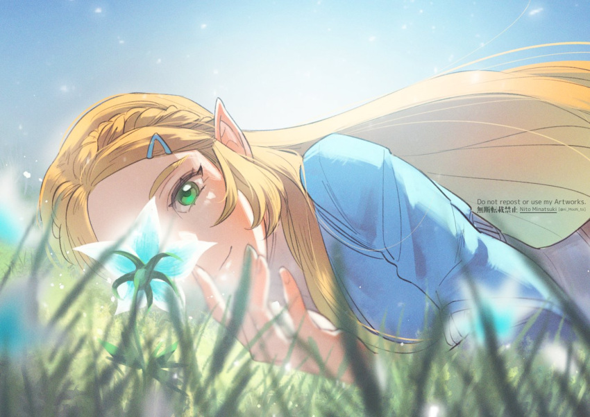 1girl, artist_name, bangs, blonde_hair, blue_shirt, blurry, blurry_foreground, braid, grass, green_eyes, hair_ornament, hairclip, long_hair, long_sleeves, lying, nito_minatsuki, on_stomach, outdoors, parted_bangs, pointy_ears, princess_zelda, shirt, sidelocks, silent_princess, smile, solo, the_legend_of_zelda, the_legend_of_zelda:_breath_of_the_wild, upper_body