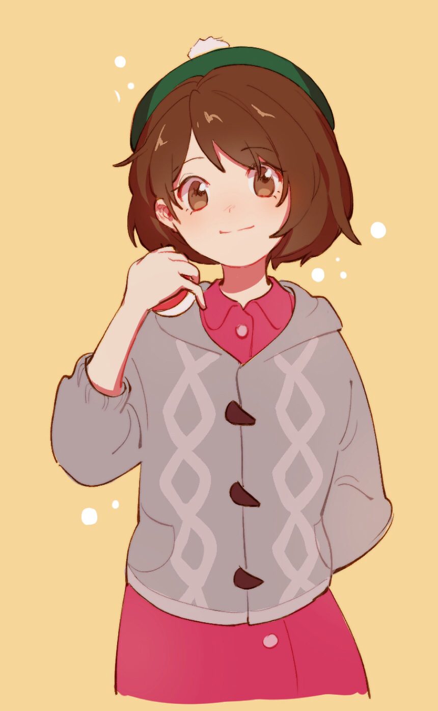 1girl, arm_behind_back, bob_cut, brown_eyes, brown_hair, buttons, cable_knit, cardigan, closed_mouth, collared_dress, commentary_request, dress, eyelashes, gloria_(pokemon), green_headwear, grey_cardigan, hand_up, hat, highres, holding, holding_poke_ball, hooded_cardigan, pink_dress, poke_ball, poke_ball_(basic), pokemon, pokemon_(game), pokemon_swsh, short_hair, simple_background, sleeves_past_elbows, smile, solo, tam_o'_shanter, yellow_background, zhongmu