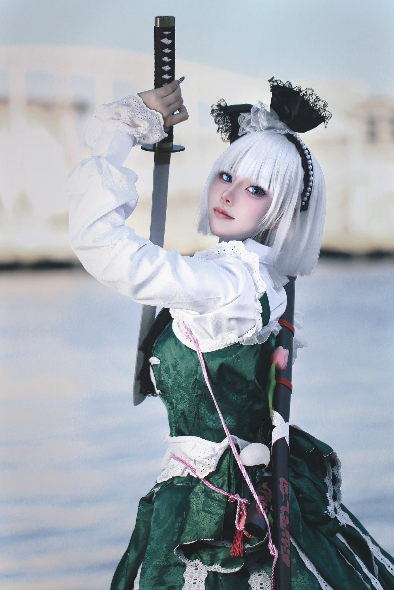 1girl, black_hairband, blue_eyes, blurry, blurry_background, breasts, closed_mouth, cosplay_photo, cowboy_shot, depth_of_field, fingernails, green_skirt, green_vest, hairband, head_tilt, highres, holding, holding_sword, holding_weapon, katana, konpaku_youmu, lace-trimmed_sleeves, lace_trim, long_fingernails, long_sleeves, looking_at_viewer, looking_to_the_side, m1yate, medium_breasts, medium_hair, photo_(medium), shirt, skirt, solo, sword, touhou, vest, weapon, white_hair, white_shirt